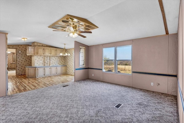 unfurnished living room with a textured ceiling, ceiling fan with notable chandelier, light hardwood / wood-style flooring, and vaulted ceiling