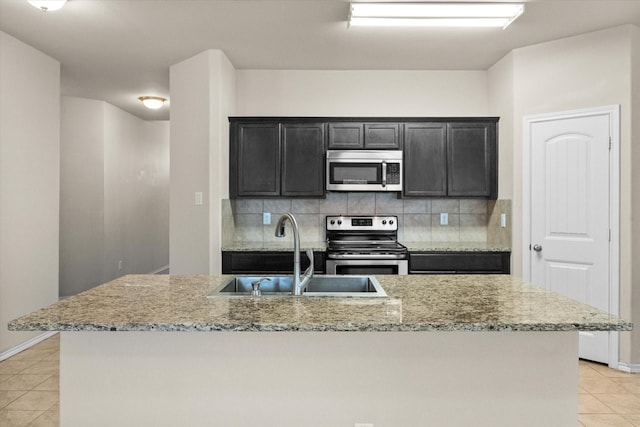 kitchen featuring sink, backsplash, light tile patterned floors, stainless steel appliances, and a center island with sink