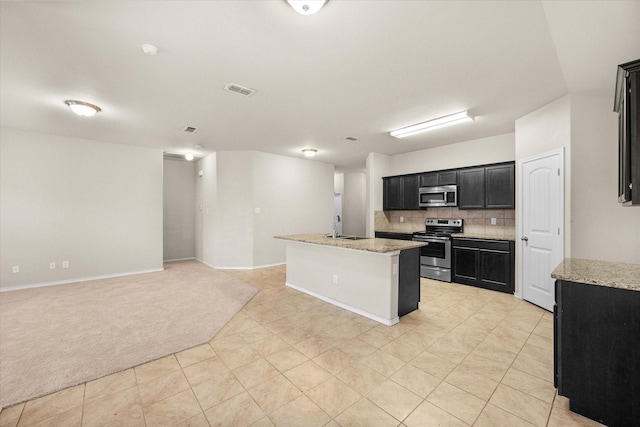 kitchen with sink, appliances with stainless steel finishes, a kitchen island with sink, light stone counters, and light carpet