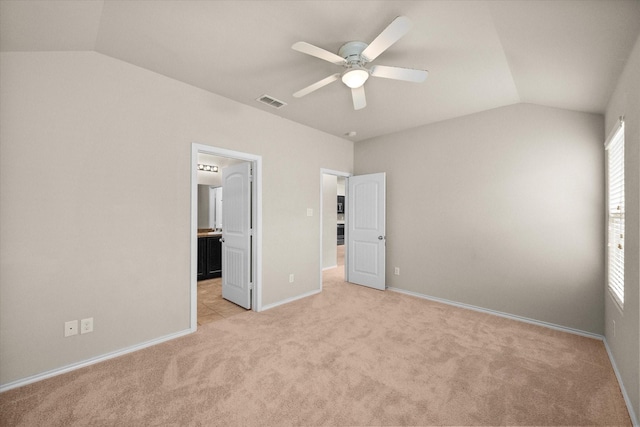 unfurnished bedroom featuring vaulted ceiling, light colored carpet, ceiling fan, and ensuite bath