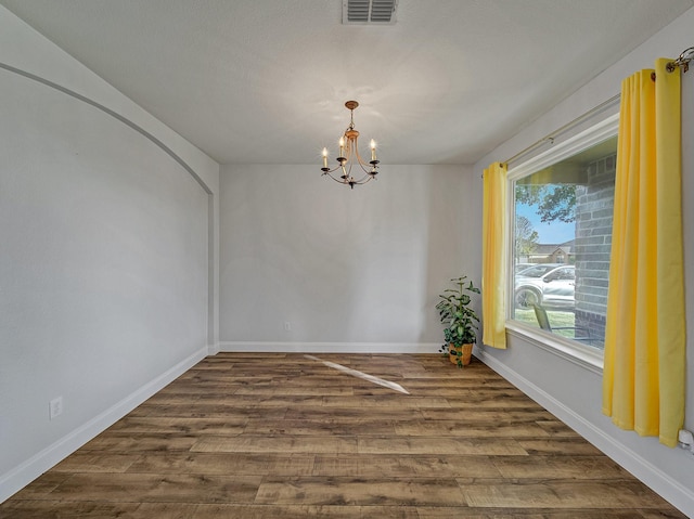 spare room with dark hardwood / wood-style flooring and an inviting chandelier