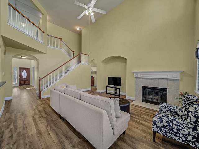 living room featuring ceiling fan, a fireplace, a high ceiling, and hardwood / wood-style flooring