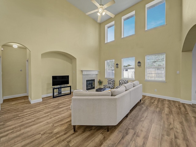 living room featuring a fireplace, a towering ceiling, light hardwood / wood-style floors, and ceiling fan