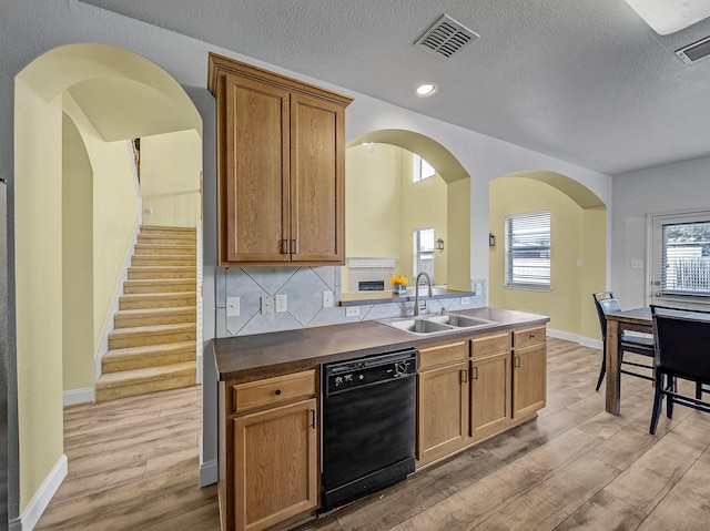 kitchen featuring sink, black dishwasher, tasteful backsplash, light hardwood / wood-style flooring, and a textured ceiling