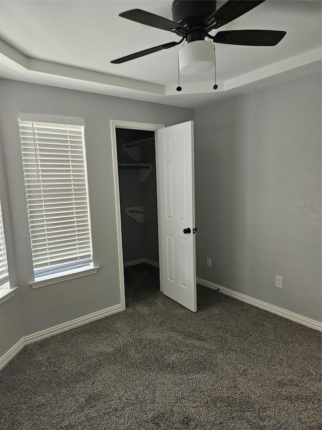 unfurnished bedroom with dark colored carpet, a walk in closet, ceiling fan, and a closet