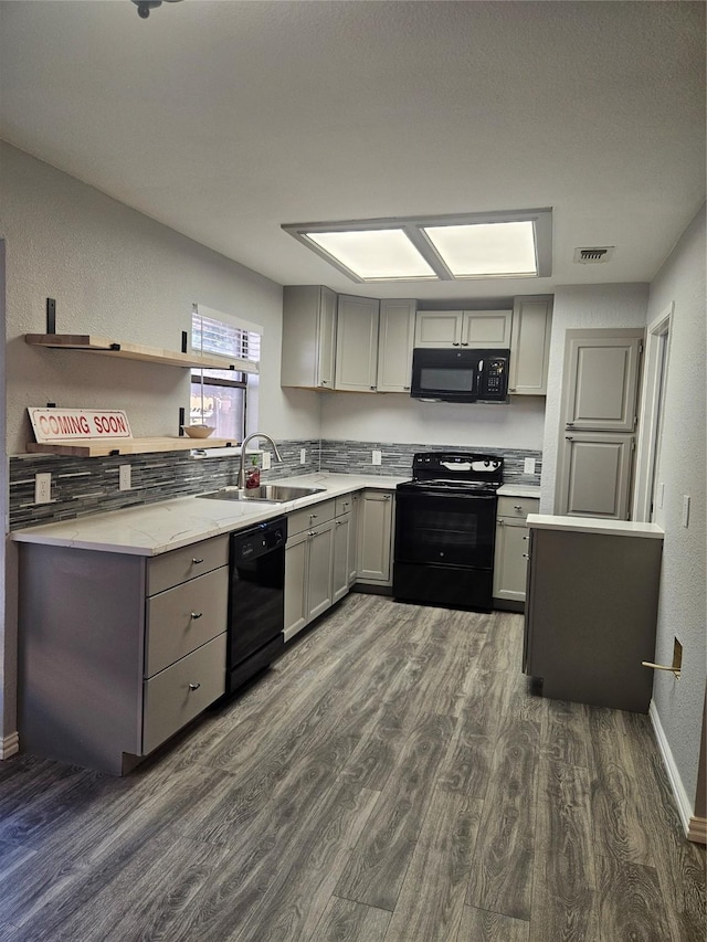 kitchen with gray cabinetry, sink, tasteful backsplash, dark hardwood / wood-style flooring, and black appliances