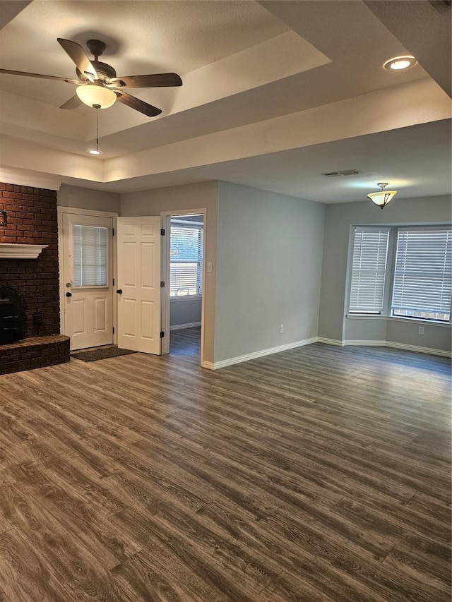 unfurnished living room with a raised ceiling, ceiling fan, and dark hardwood / wood-style flooring