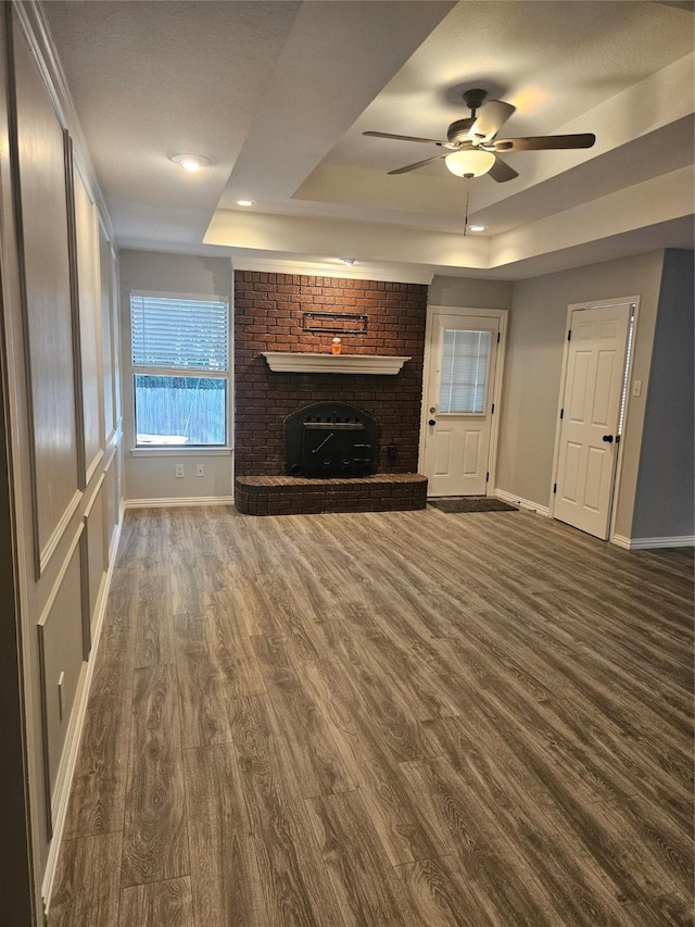 unfurnished living room featuring ceiling fan, a brick fireplace, dark hardwood / wood-style flooring, and a tray ceiling