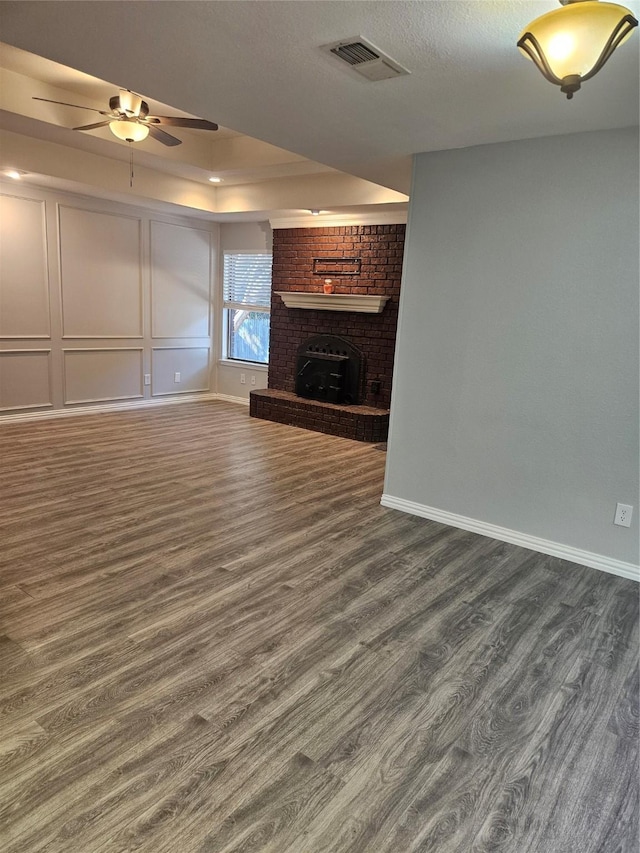 unfurnished living room with a textured ceiling, dark hardwood / wood-style floors, a brick fireplace, and ceiling fan