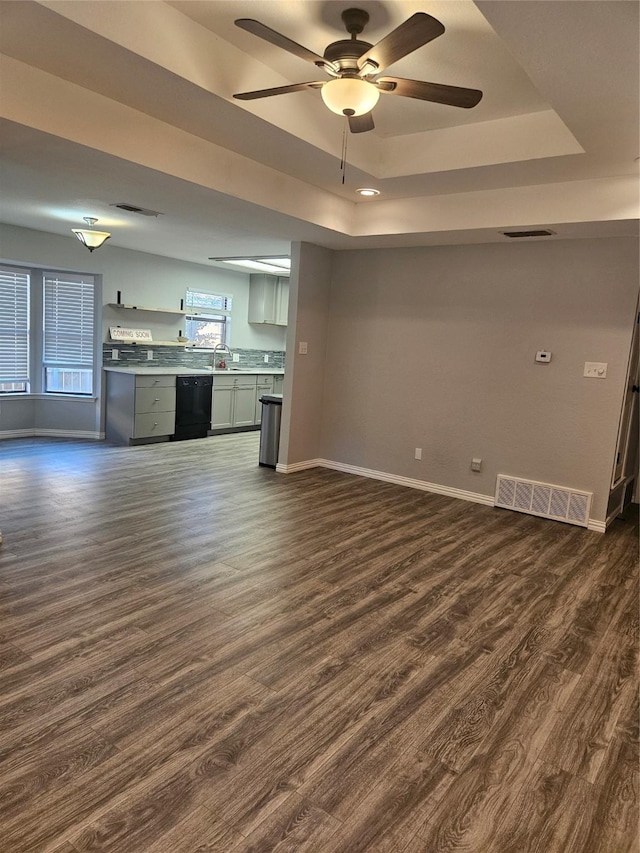 unfurnished living room featuring ceiling fan, a tray ceiling, dark hardwood / wood-style flooring, and sink