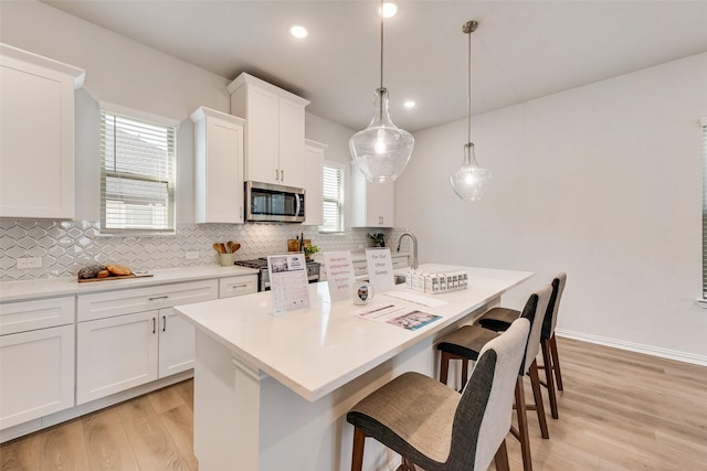 4557 Ward St, North Richland Hills, TX 76180 - kitchen with an island with sink, tasteful backsplash, a kitchen breakfast bar, appliances with stainless steel finishes, and light wood-style flooring