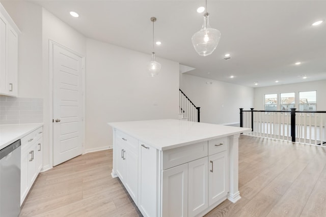 kitchen with a center island, hanging light fixtures, light wood-type flooring, stainless steel dishwasher, and white cabinets