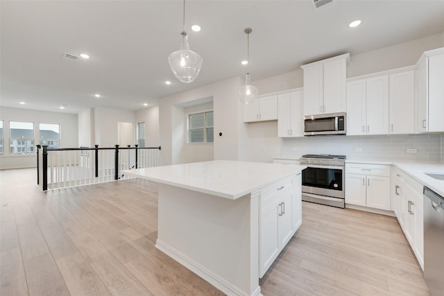 kitchen with hanging light fixtures, stainless steel appliances, white cabinets, and a kitchen island