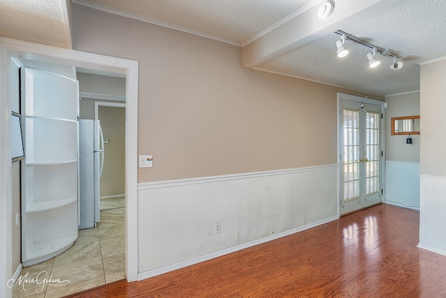 spare room with french doors, rail lighting, crown molding, wood-type flooring, and a textured ceiling