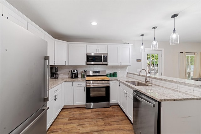 kitchen with pendant lighting, white cabinets, sink, kitchen peninsula, and stainless steel appliances