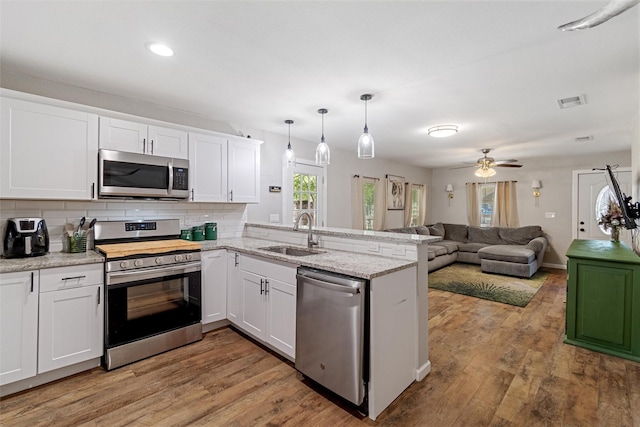 kitchen with pendant lighting, sink, appliances with stainless steel finishes, white cabinetry, and kitchen peninsula