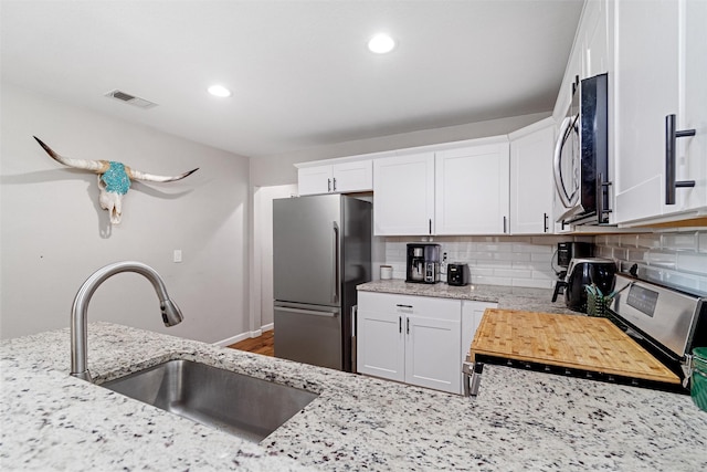 kitchen with appliances with stainless steel finishes, light stone countertops, sink, and white cabinets