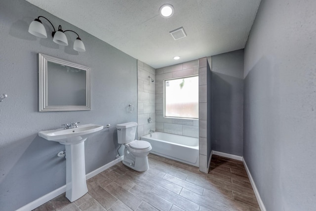 bathroom with tiled shower / bath combo, toilet, and a textured ceiling