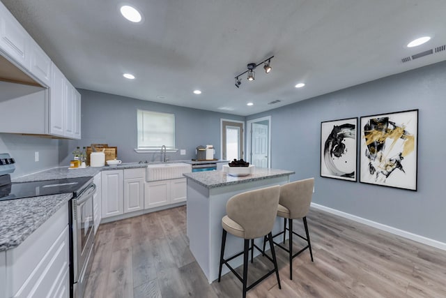 kitchen featuring sink, stainless steel appliances, a kitchen island, white cabinets, and light wood-type flooring