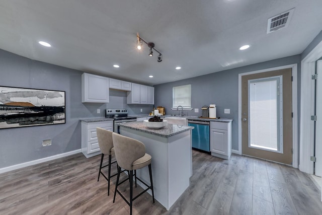 kitchen featuring a center island, white cabinets, appliances with stainless steel finishes, light hardwood / wood-style floors, and a breakfast bar area