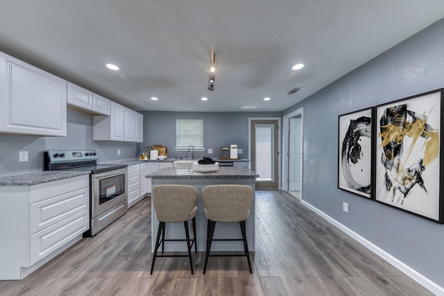 kitchen featuring white cabinetry, stainless steel electric range oven, a kitchen island, and wood-type flooring