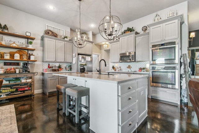 kitchen featuring gray cabinets, a kitchen island with sink, backsplash, and appliances with stainless steel finishes