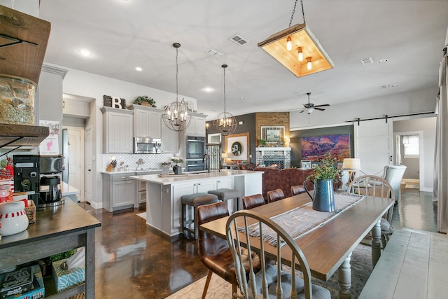 dining area with a fireplace, a barn door, and ceiling fan