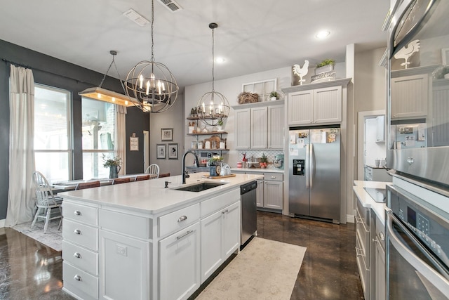 kitchen featuring sink, stainless steel appliances, tasteful backsplash, decorative light fixtures, and a center island with sink