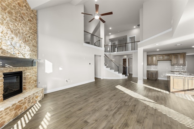 unfurnished living room with stairway, dark wood-style flooring, a stone fireplace, and baseboards