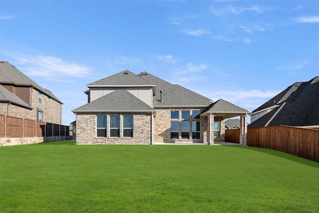 rear view of property with a yard, brick siding, a shingled roof, and a fenced backyard