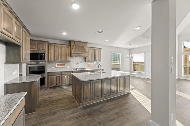 kitchen featuring an island with sink, custom range hood, stainless steel appliances, and a sink