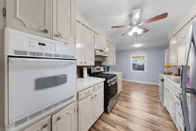 kitchen with appliances with stainless steel finishes, white cabinets, a textured ceiling, and light hardwood / wood-style flooring