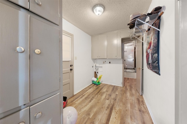 laundry area featuring cabinets, a textured ceiling, and light hardwood / wood-style flooring