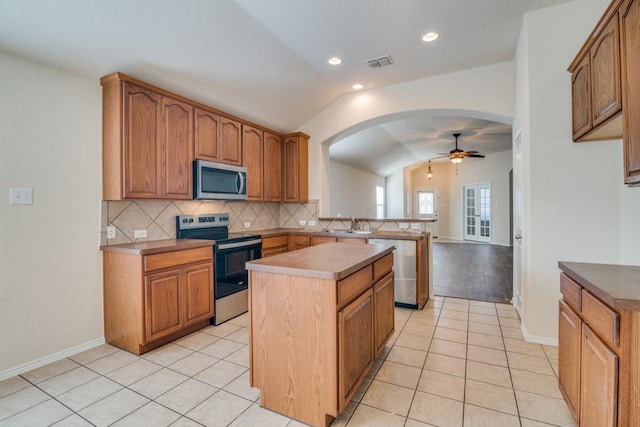 kitchen with ceiling fan, a center island, stainless steel appliances, vaulted ceiling, and light tile patterned floors