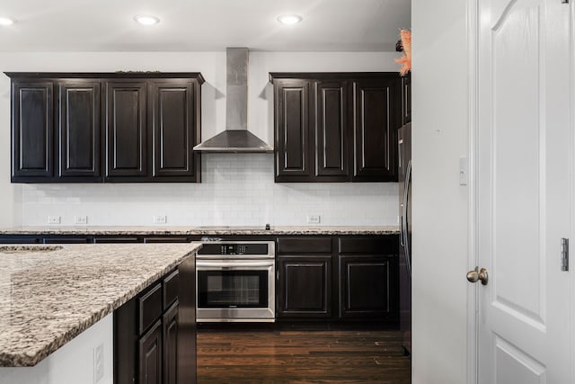 kitchen featuring tasteful backsplash, wall chimney range hood, stainless steel appliances, and dark wood-type flooring