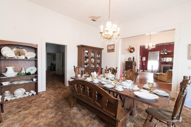 dining area with dark colored carpet, ceiling fan with notable chandelier, and a fireplace