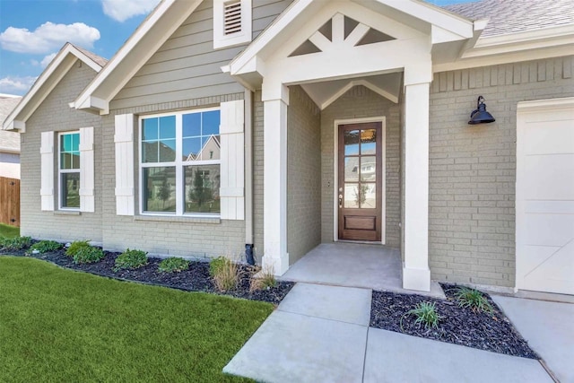 view of exterior entry featuring a garage, a yard, brick siding, and a shingled roof