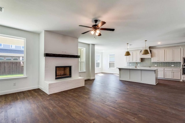 kitchen with dark hardwood / wood-style flooring, a brick fireplace, a kitchen island with sink, pendant lighting, and white cabinets