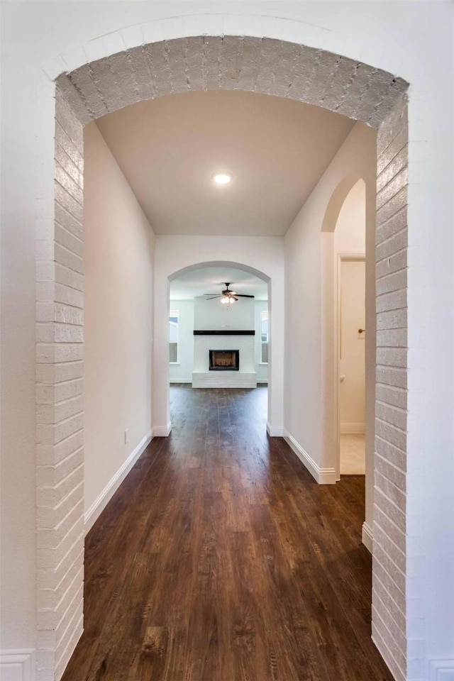 hallway featuring dark wood-style floors, arched walkways, and baseboards