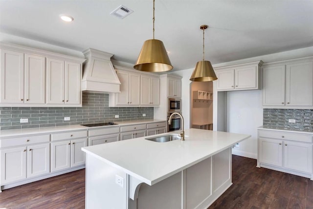 kitchen with premium range hood, a sink, visible vents, light countertops, and a center island with sink