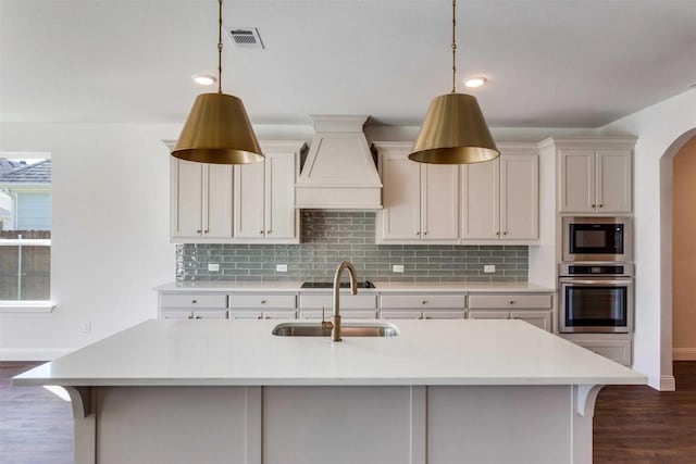 kitchen with light countertops, custom range hood, hanging light fixtures, stainless steel oven, and a sink