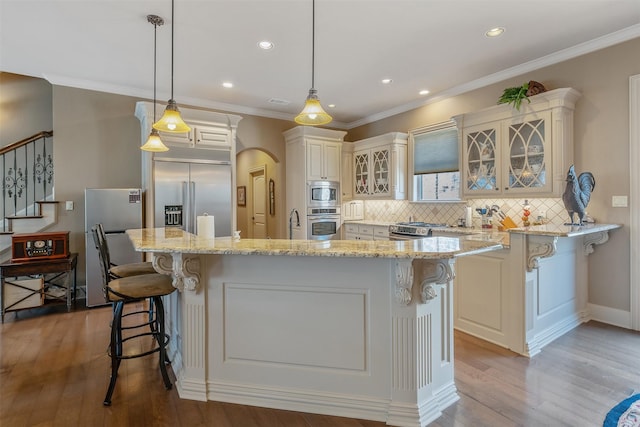 kitchen featuring a breakfast bar, hanging light fixtures, a center island, built in appliances, and light stone counters