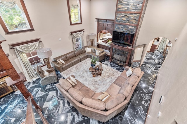 living room with a towering ceiling, a healthy amount of sunlight, and a tiled fireplace