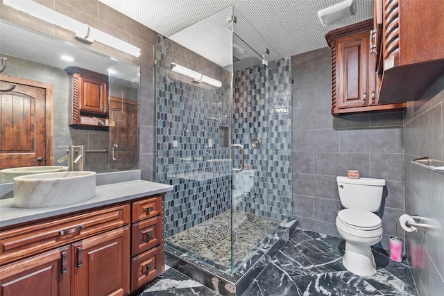 bathroom with vanity, toilet, tile walls, and a shower with shower door