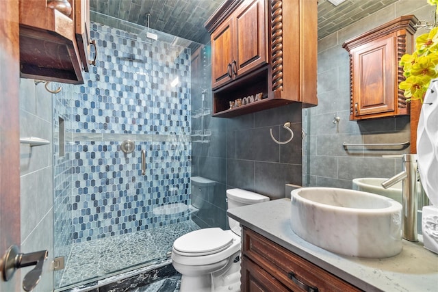 bathroom with vanity, toilet, a shower with door, and tile walls