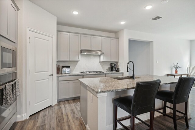 kitchen featuring light wood-type flooring, a center island with sink, light stone counters, and sink