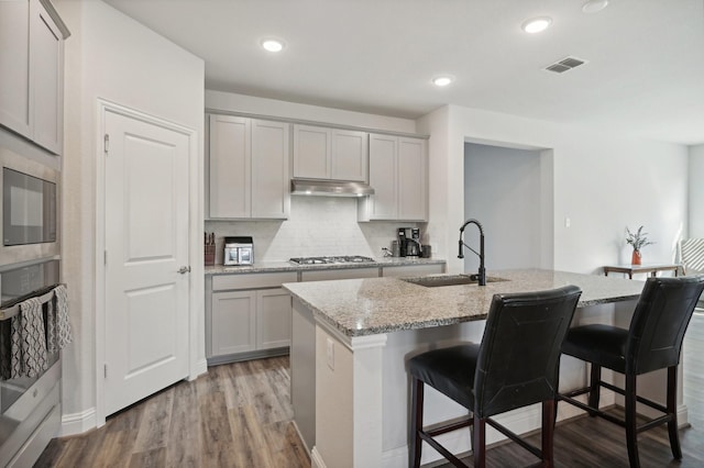 kitchen featuring sink, a kitchen bar, light stone countertops, and a center island with sink