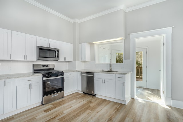 kitchen featuring sink, white cabinets, ornamental molding, stainless steel appliances, and light hardwood / wood-style flooring