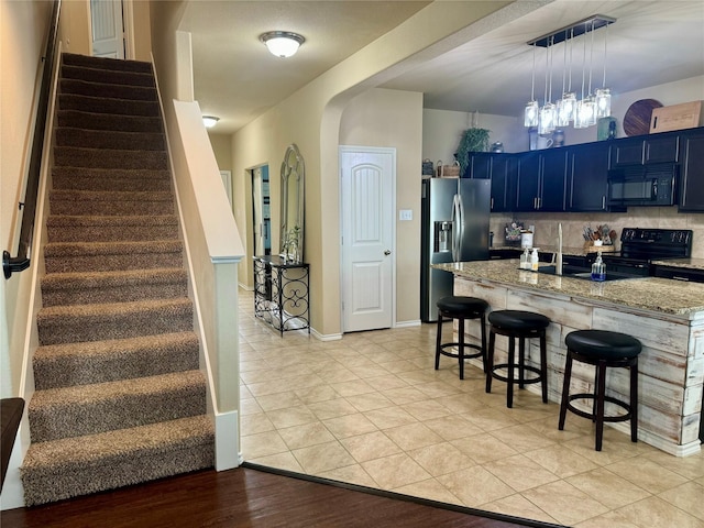 kitchen featuring a breakfast bar area, blue cabinetry, backsplash, light stone counters, and black appliances