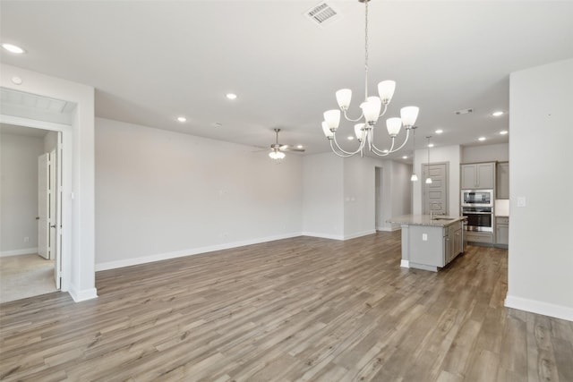 unfurnished living room featuring sink, ceiling fan with notable chandelier, and light wood-type flooring